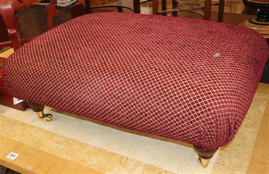 A large rectangular red upholstered stool on brass castors W.90cm